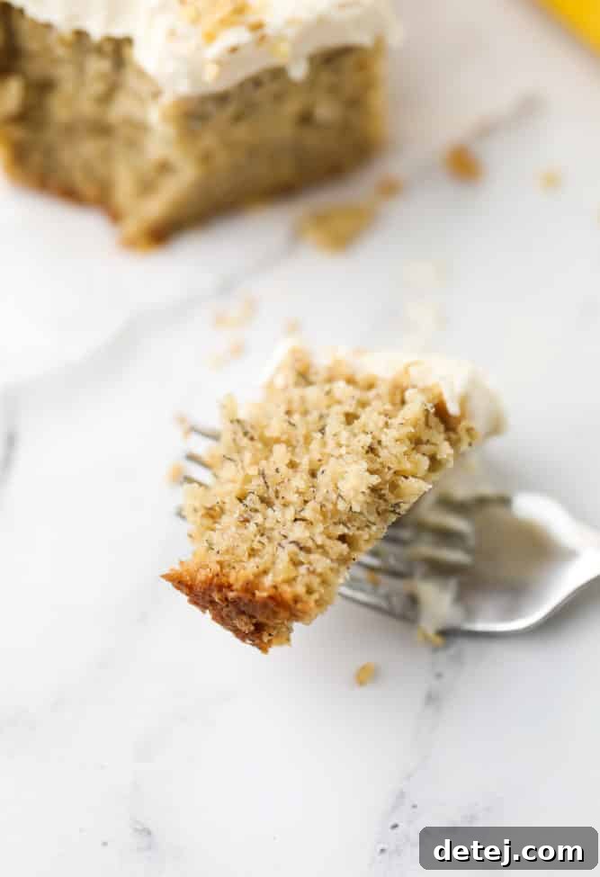 A fork lifts a piece of vegan banana cake, showcasing its incredibly moist and tender texture, with visible specks of banana throughout.