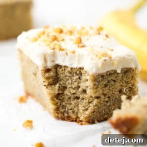 A square image of a slice of vegan banana cake with creamy frosting and chopped walnuts on top, ready to serve.
