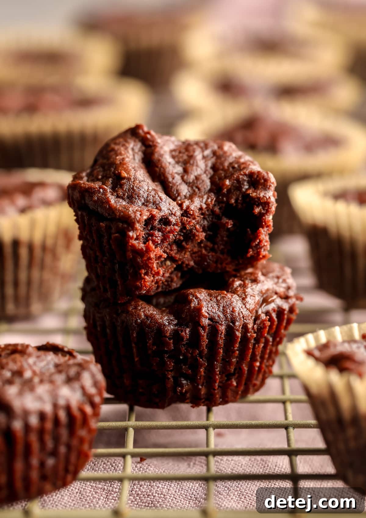 A perfectly baked brownie bite with a corner taken out, revealing its fudgy interior, resting on another brownie bite with more in the blurred background.