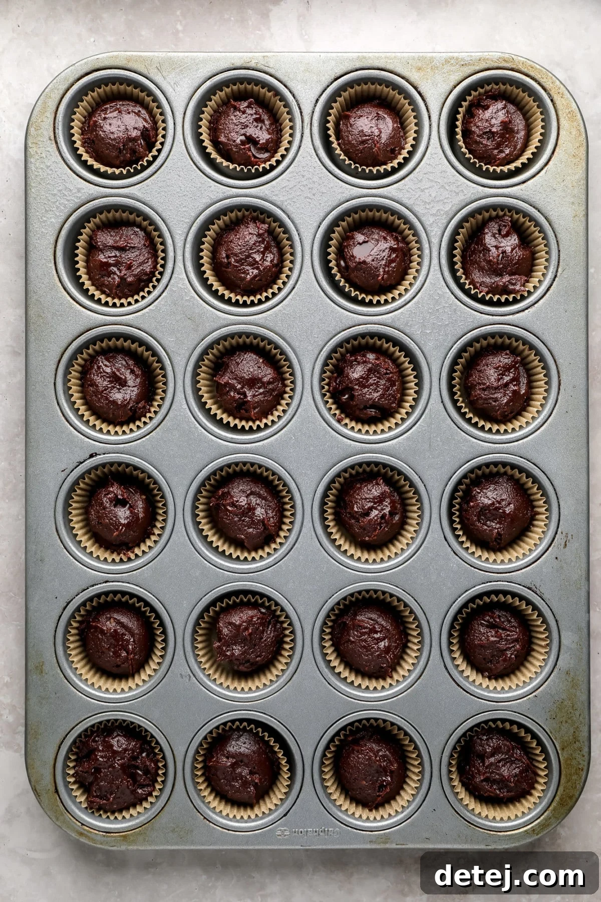 Close-up shot of uncooked chocolate brownie batter neatly portioned into mini muffin cups lined with paper, ready for baking.