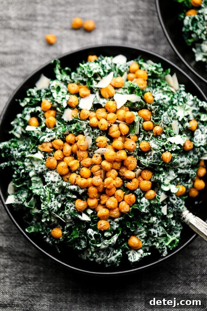 Close up of a vibrant Kale Caesar Salad in a black bowl, topped generously with golden-brown chickpea croutons and a sprinkle of vegan parmesan.