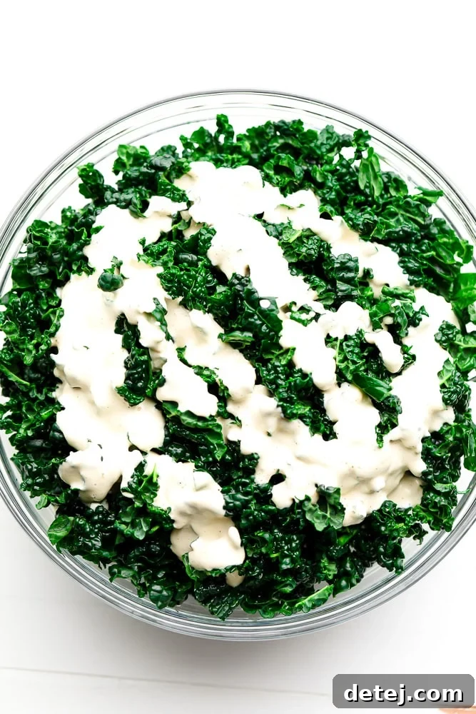 A large bowl of fresh kale, perfectly coated with a creamy white Caesar dressing, showcasing the rich texture before adding toppings.