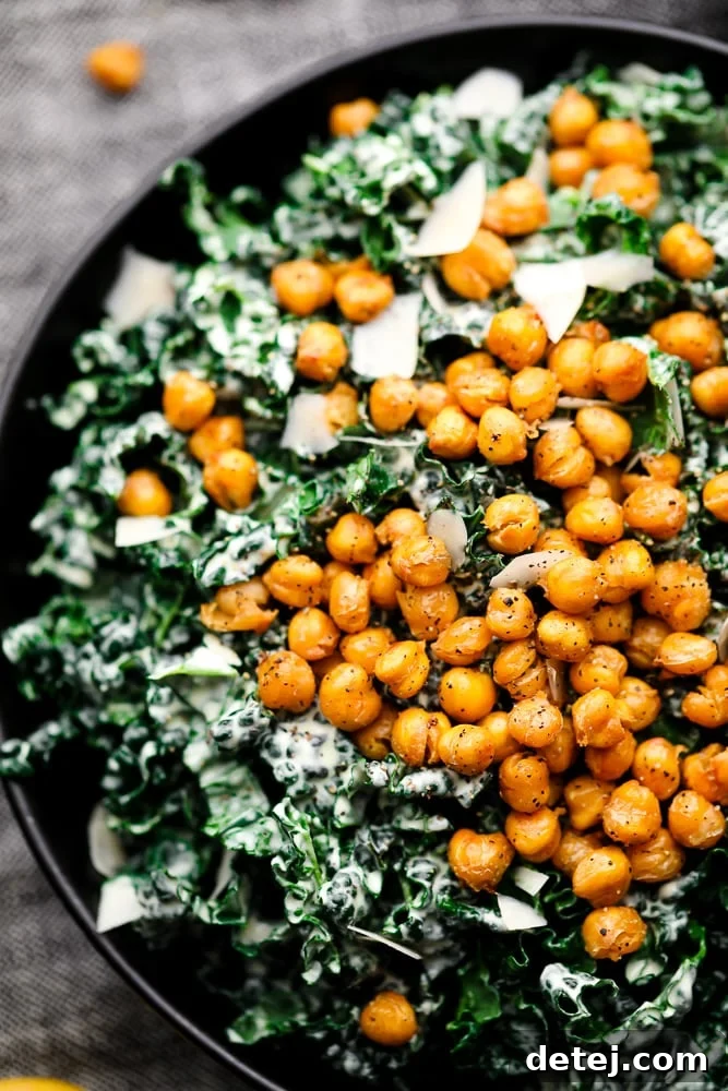 A close-up of a beautifully presented Kale Caesar Salad in a black bowl, highlighting the texture of the massaged kale and the generous topping of chickpea croutons.