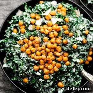Close up of a vibrant green Caesar salad in a black bowl, generously topped with golden chickpea croutons.
