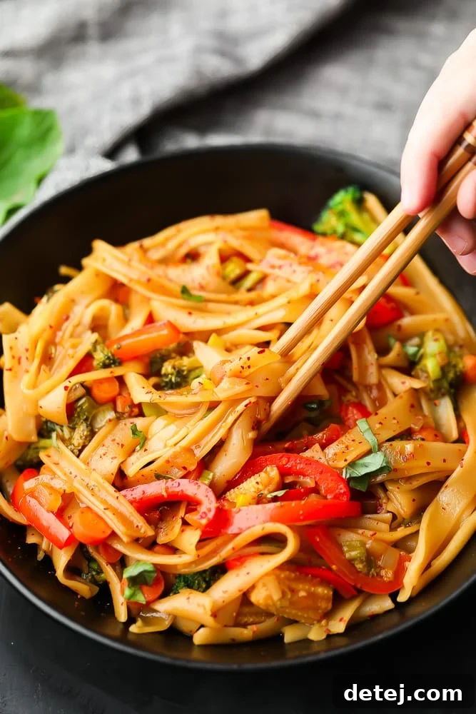 close-up of chopsticks holding a tangle of vegan drunken noodles from a black bowl