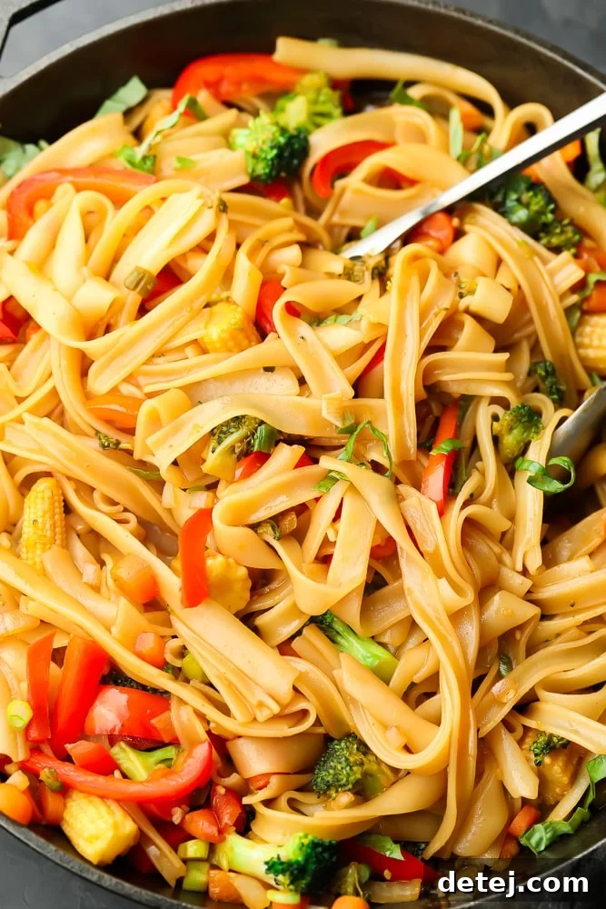 pan full of stir-fried vegan drunken noodles and tongs for serving