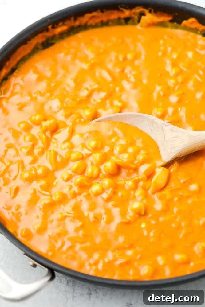 wooden spoon stirring an orange sauce with chickpeas in a large skillet