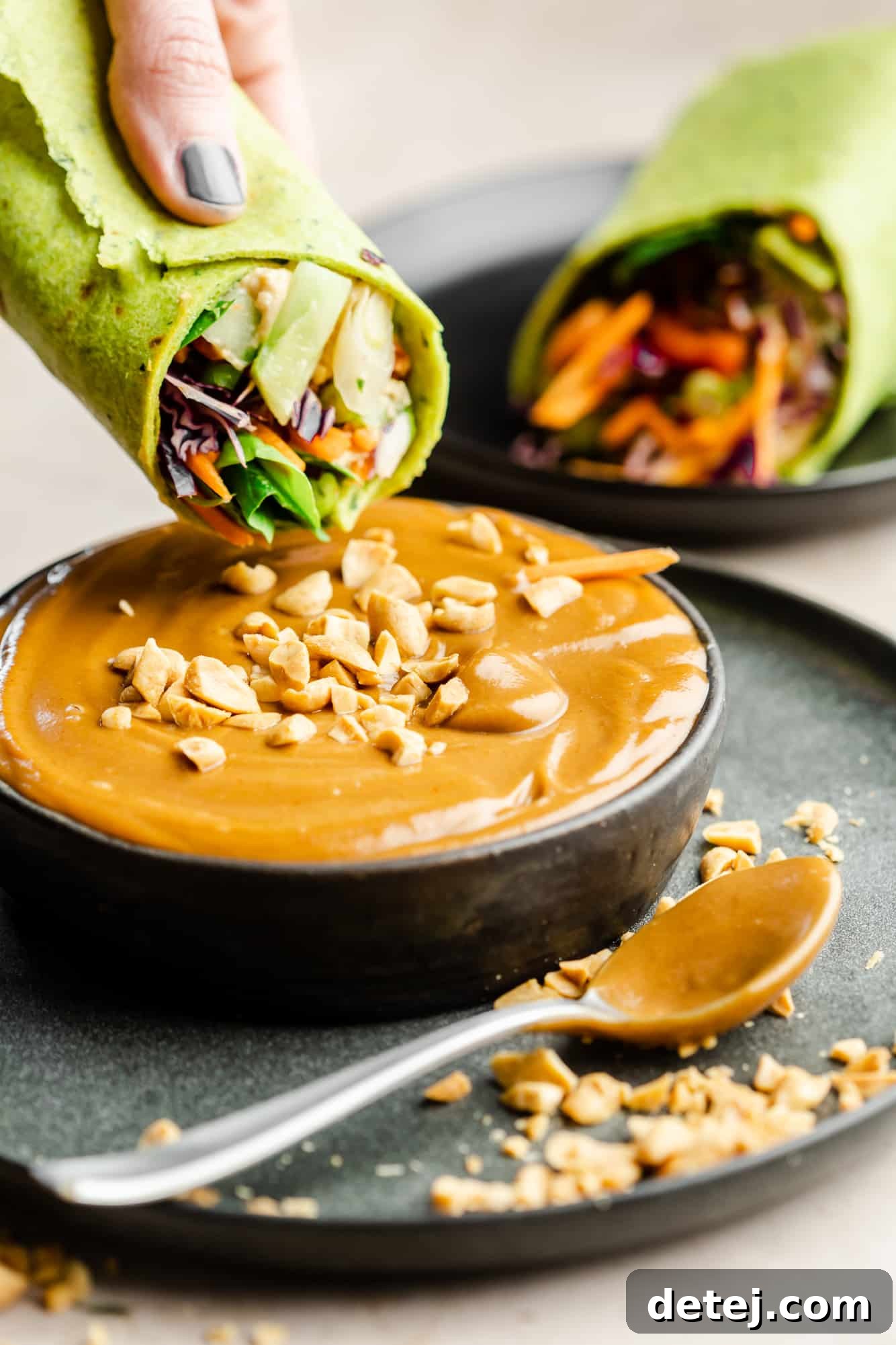 A fresh vegetable wrap being dipped into a luscious bowl of homemade peanut sauce, highlighting its creamy texture.