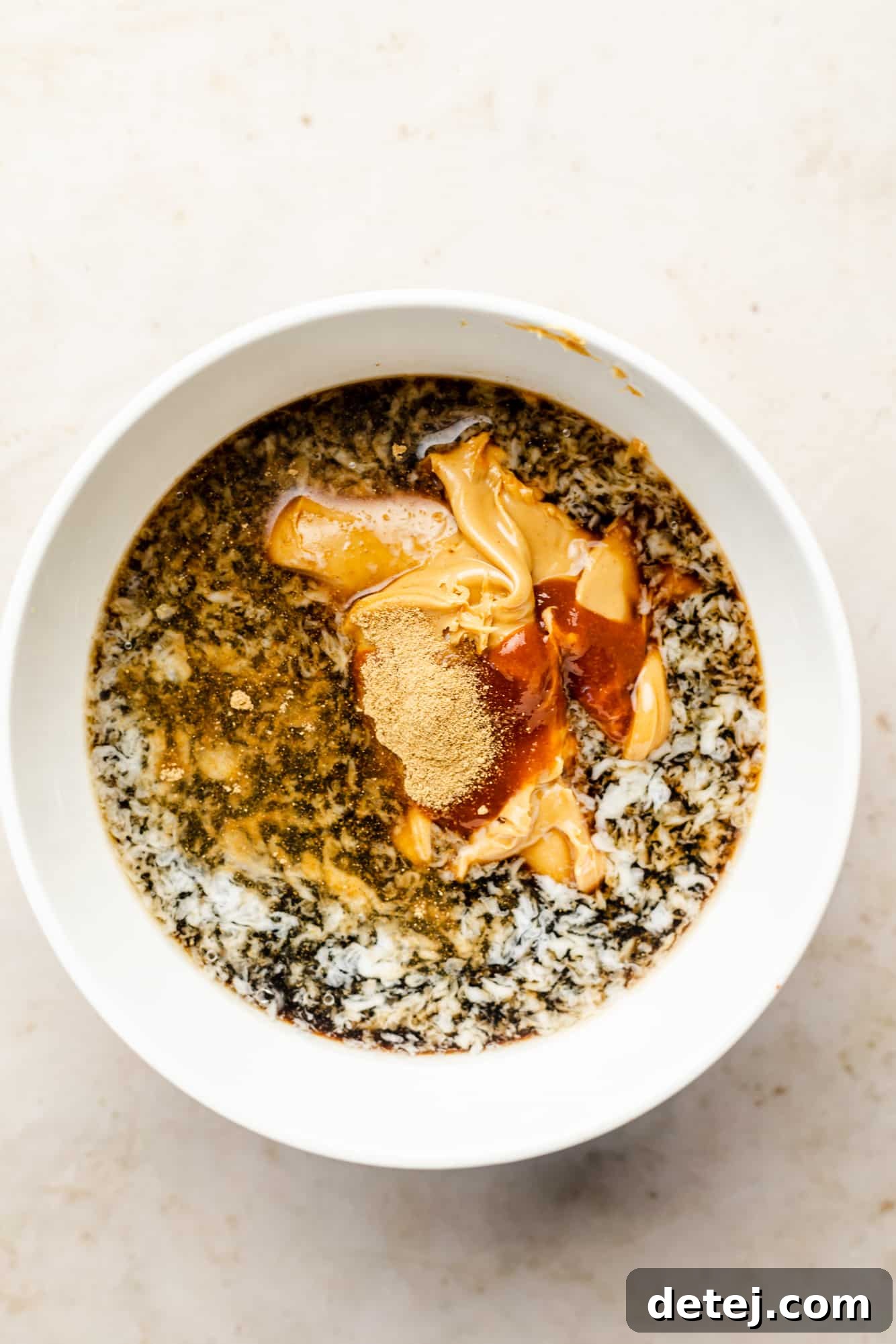 All the dry and liquid ingredients for peanut sauce (excluding thinning liquid) are mixed together in a white bowl, awaiting whisking.