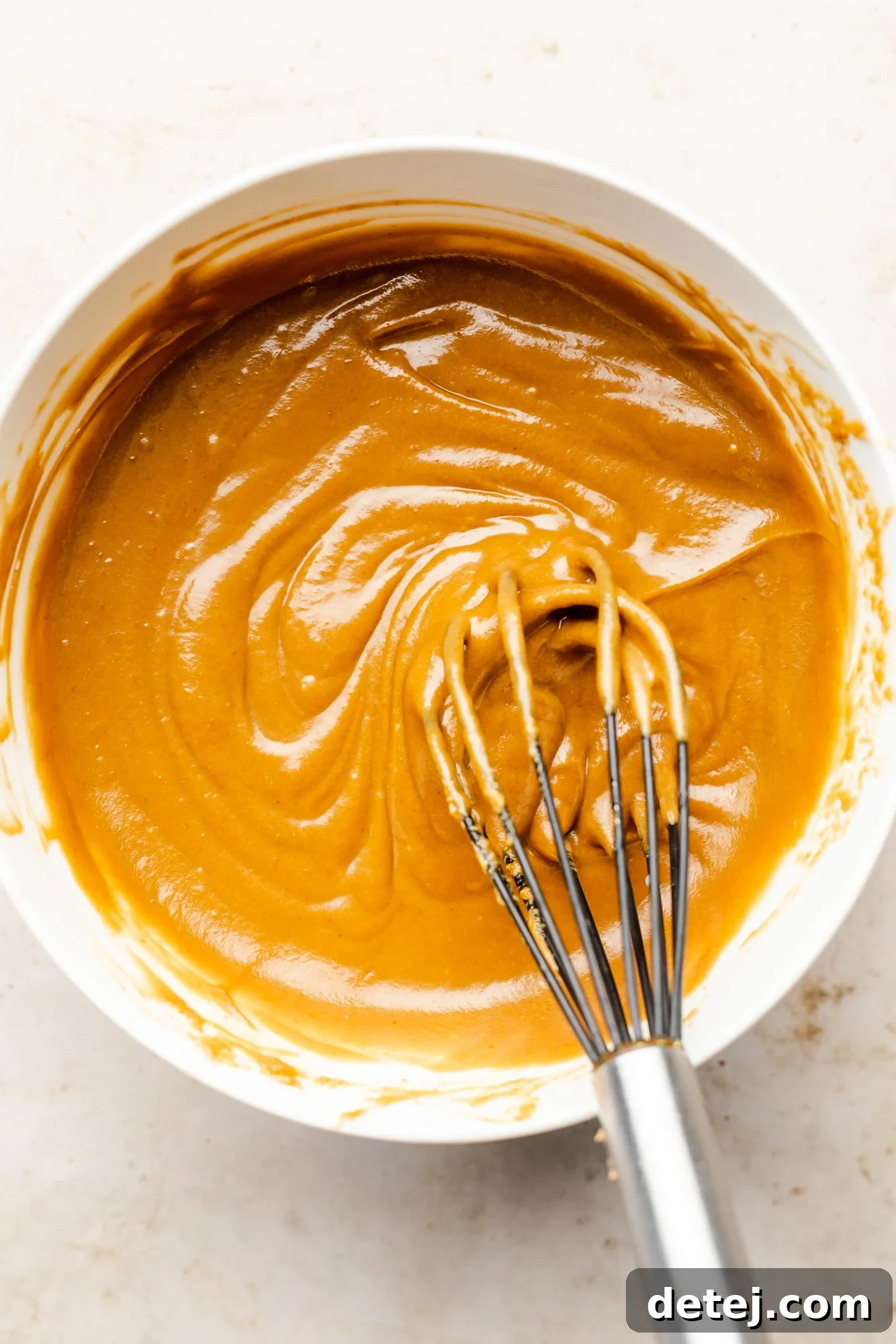 A close-up of a whisk blending the last bit of ingredients in a white bowl, resulting in a perfectly smooth and rich peanut sauce.