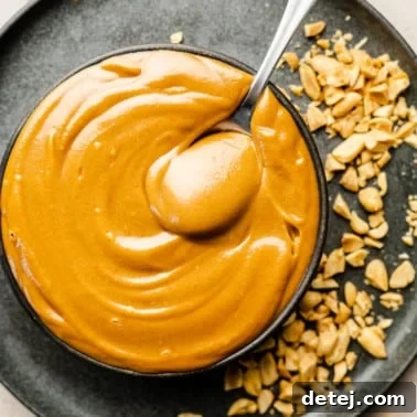 a spoon in a bowl of peanut sauce on top of a black plate with crushed peanuts.