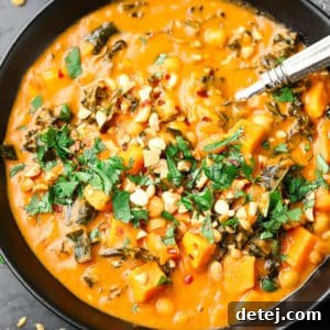 black bowl filled with orange peanut soup with cilantro and peanuts on top
