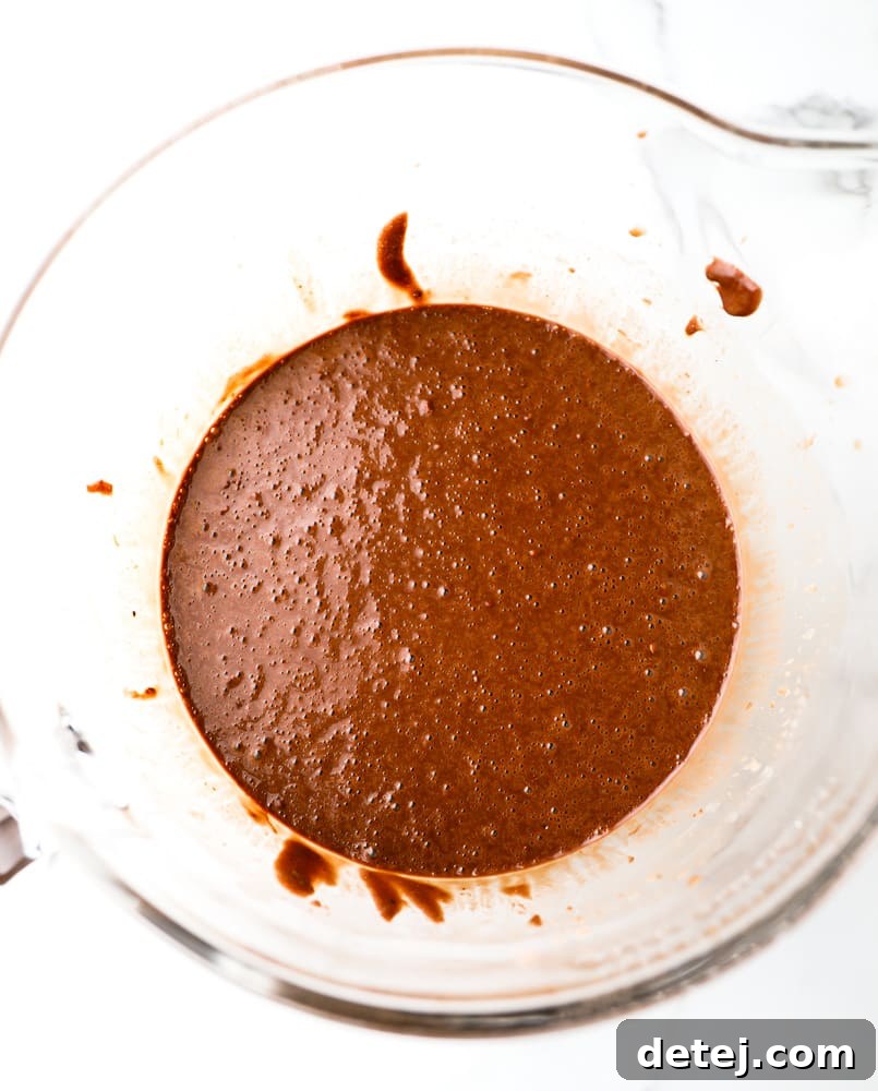 Large glass bowl filled with rich, glossy gluten-free vegan chocolate cake batter, ready for baking.