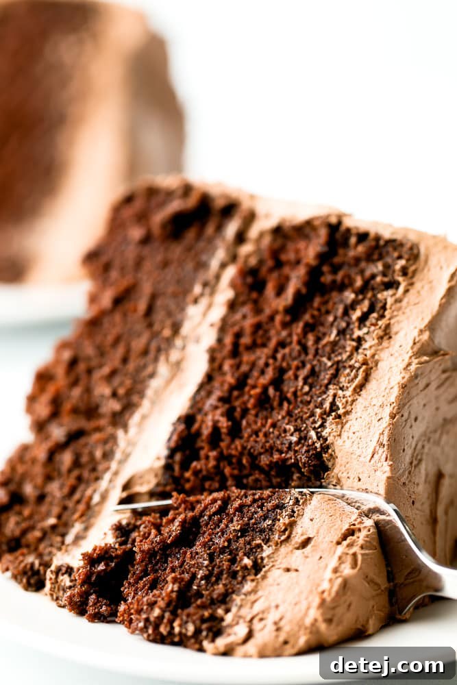 Close up of a fork taking a bite out of a frosted slice of gluten-free vegan chocolate cake, showing the soft, irresistible texture.
