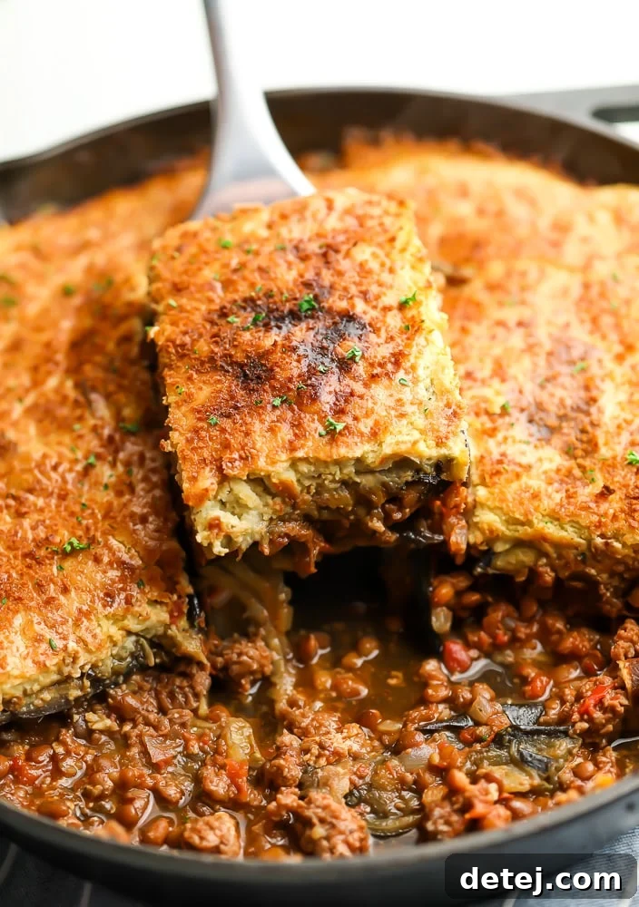 Spoon taking a slice of golden brown moussaka out of a baking dish