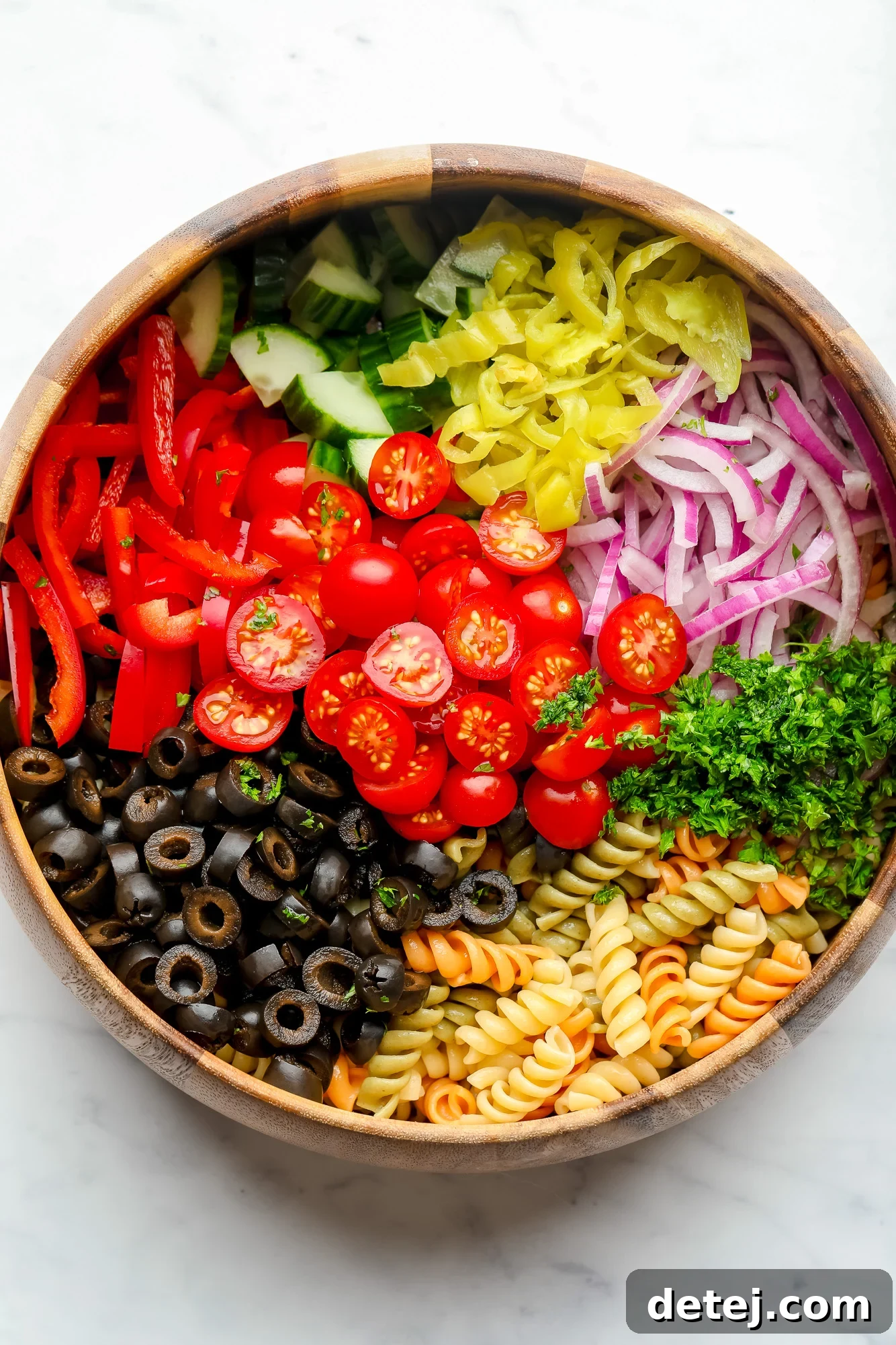 wood bowl on white background with pasta and vegetables not yet mixed for vegan pasta salad