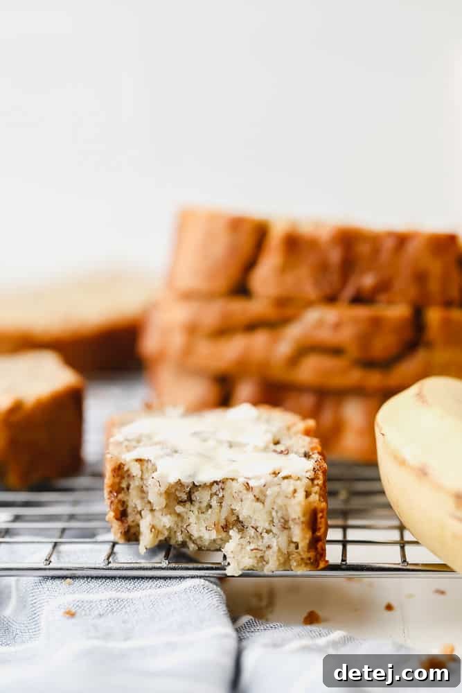 A perfectly buttered and bitten slice of homemade gluten-free vegan banana bread rests on a cooling rack, showcasing its moist texture.