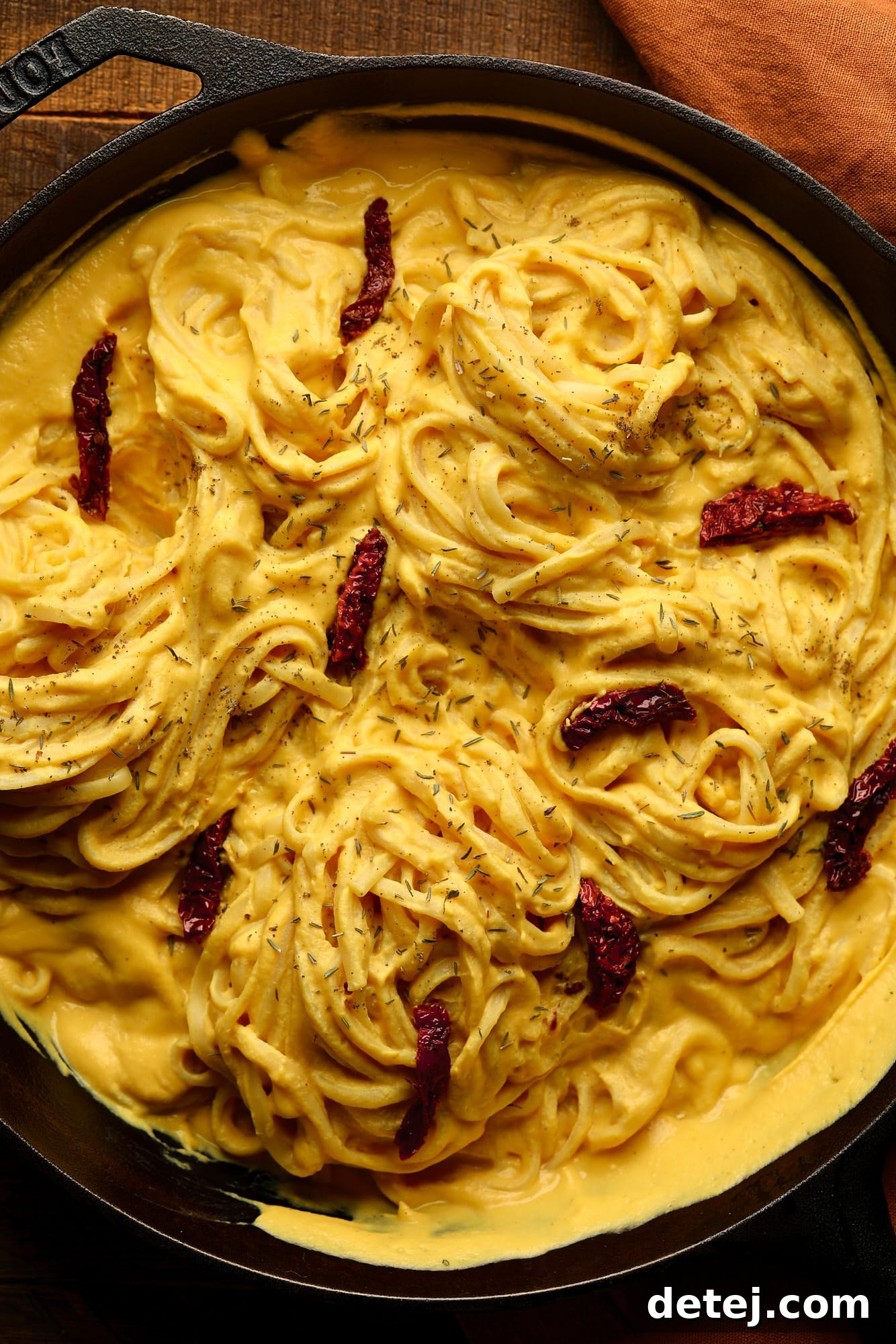 Velvety Butternut Pasta Sauce 6 pan with yellow cream pasta and sun dried tomatoes, orange towel in wooden background
