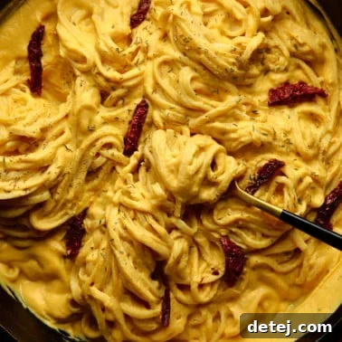 square image of long noodles coated in creamy yellow sauce