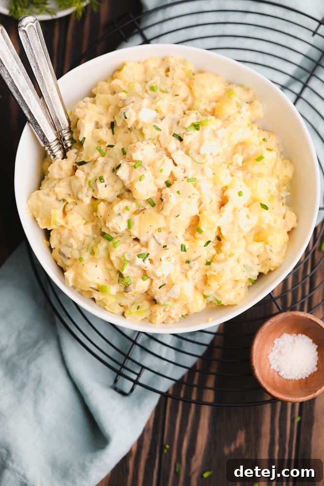 A beautifully presented bowl of vegan potato salad garnished with fresh chives, sitting on a black round cooling rack, ready to be served.