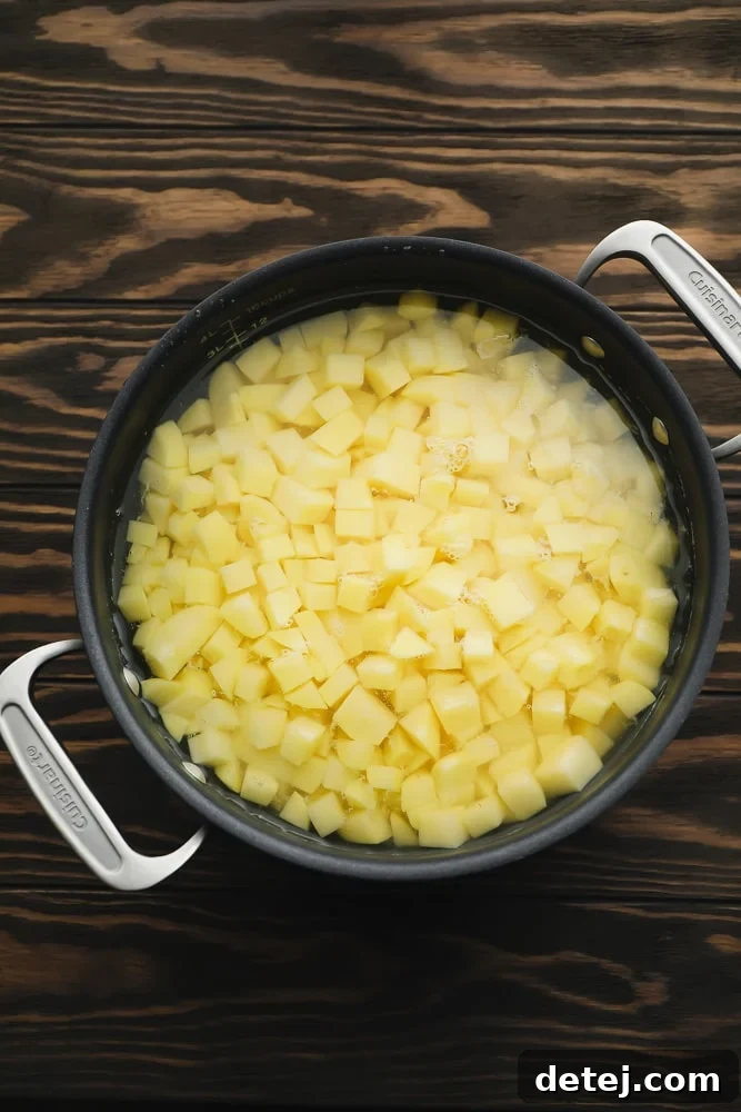 A black pot filled with golden yellow diced potatoes, perfectly boiled and ready for the next step, set against a rustic wood background.