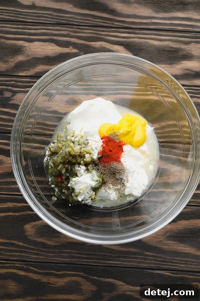 A glass bowl showcasing the unstirred dressing ingredients – creamy vegan mayo, bright relish, and spices – awaiting to be combined.