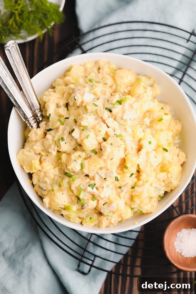 A large bowl of creamy vegan potato salad, garnished with fresh herbs and featuring two forks, presented on a black round cooling rack.