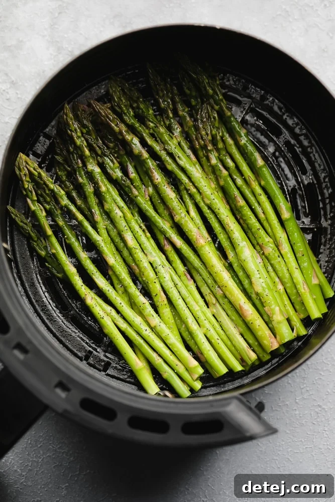 seasoned raw asparagus in an air fryer basket