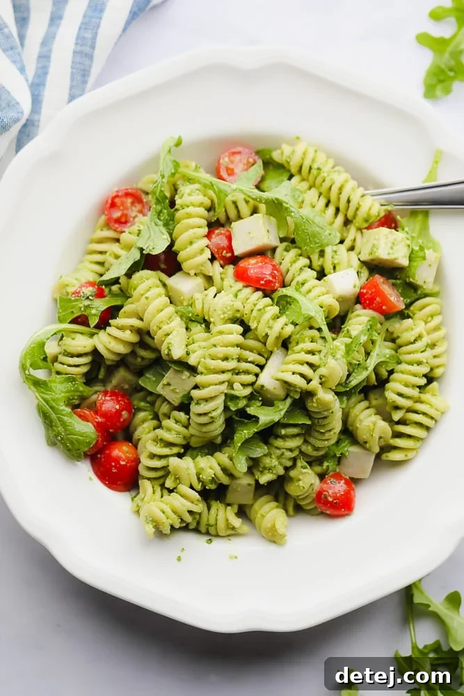 pesto pasta salad with tomatoes in a white bowl, garnished with fresh herbs