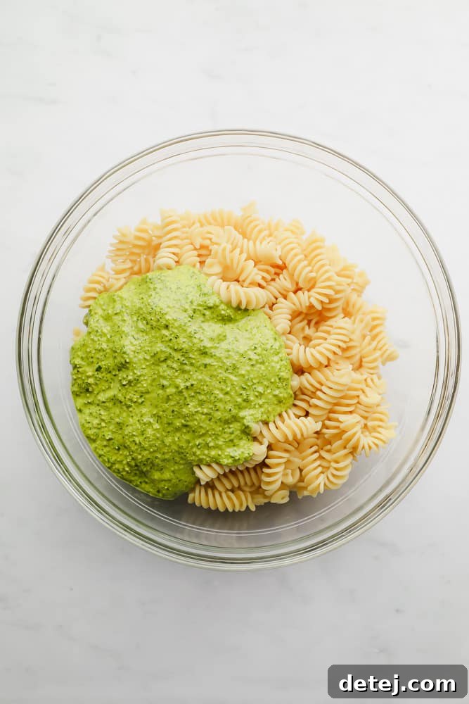 pesto poured on top of cooked pasta in a glass bowl, ready to be mixed