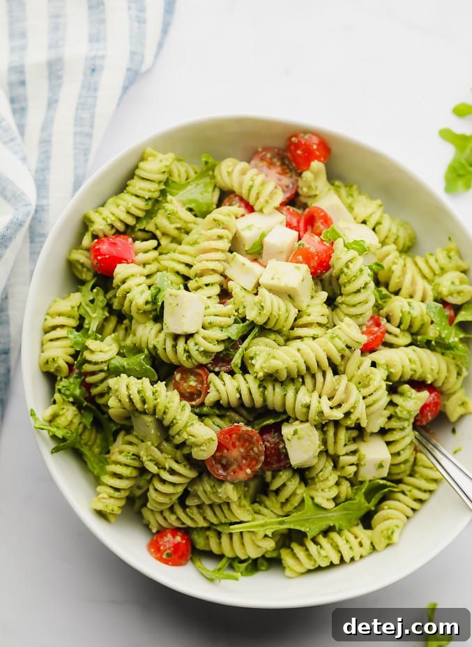green pasta salad with tomatoes in a white bowl, ready to be served at a picnic