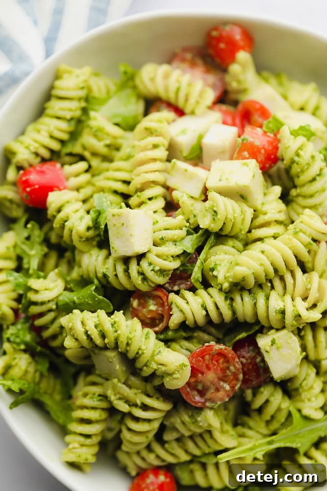 close up on pesto pasta salad in a white bowl, showing texture and ingredients