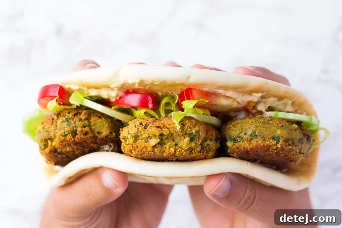 Hands holding a flatbread filled with vegan falafel and fresh vegetables, ready to eat