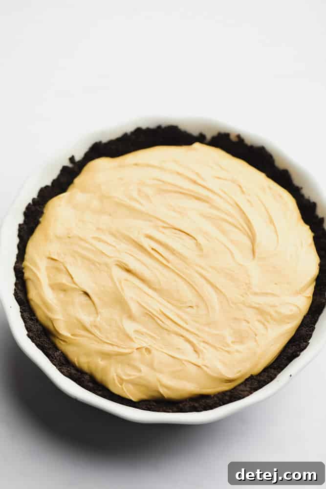 A beautifully presented whole vegan peanut butter pie, showcasing its smooth, light brown filling in a dark chocolate Oreo crust, garnished with luscious toppings and ready to be sliced.