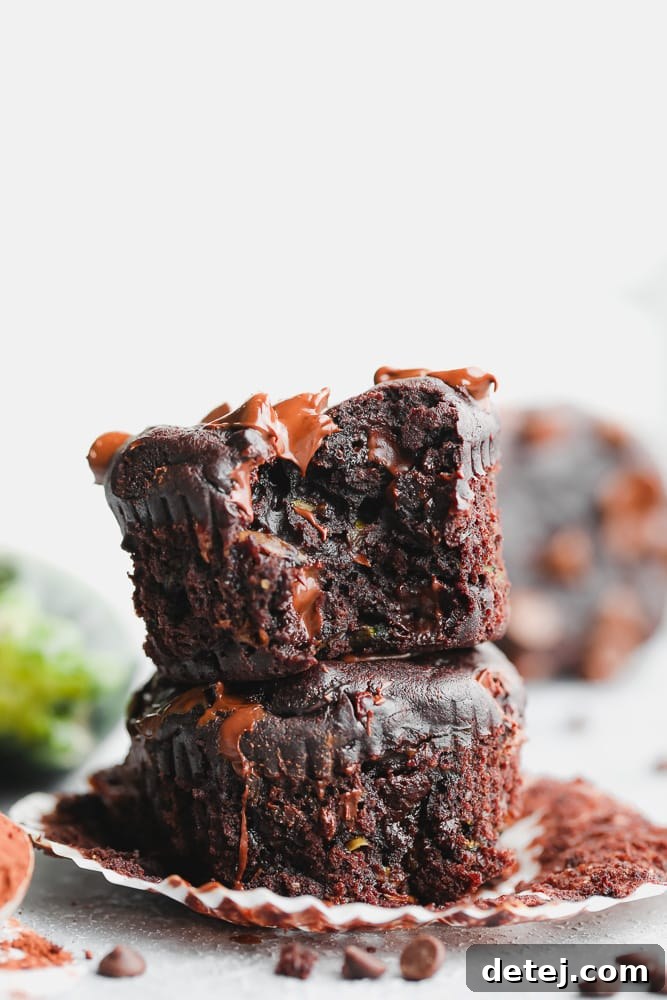 Two decadent vegan chocolate zucchini muffins, generously studded with chocolate chips, stacked invitingly on a rustic wooden surface, ready to be enjoyed.