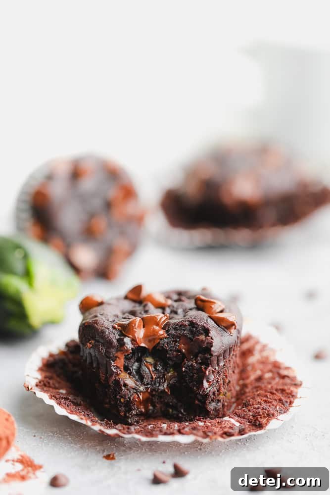 A vegan chocolate muffin, unwrapped and with a delectable bite taken out, revealing its moist, tender interior studded with melted chocolate chips, resting on a rustic wooden board.