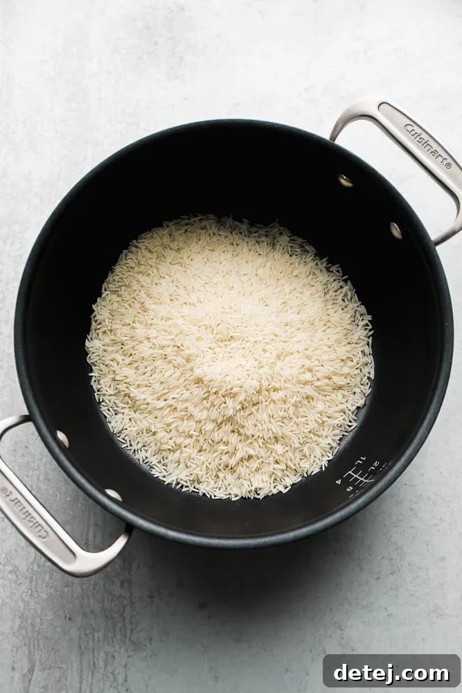 Uncooked white Basmati rice grains displayed in a black pot, ready for rinsing and cooking.