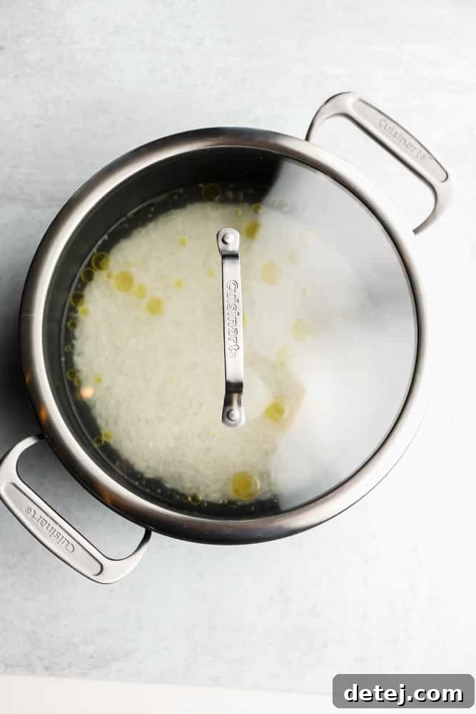 White Basmati rice, oil, and water mixture in a black pot, now covered with a glass lid, ready for simmering.
