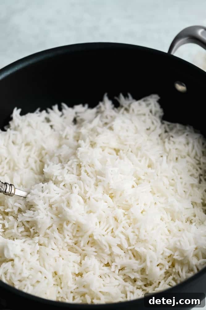 Close-up of a fork gently fluffing white Basmati rice in a black pot, illustrating the final step before serving.