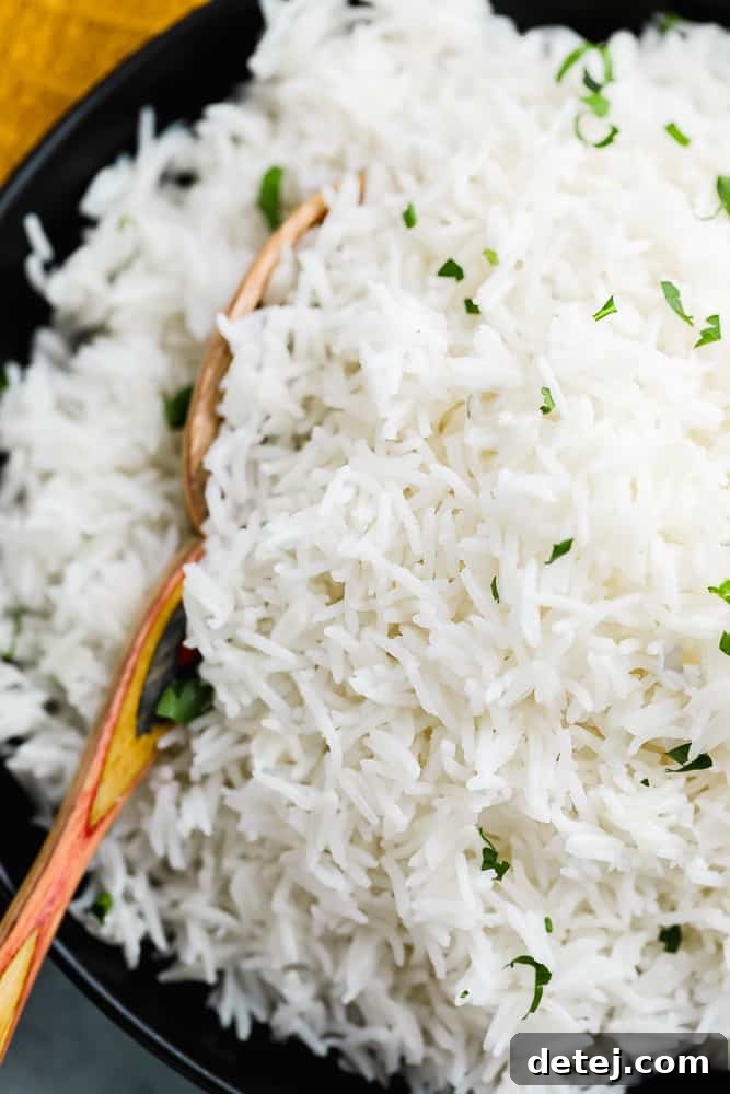 Close-up of a wooden spoon scooping a generous portion of fluffy white Basmati rice out of a black bowl.