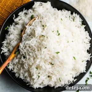 Wooden spoon taking a scoop of white Basmati rice out of a black bowl.