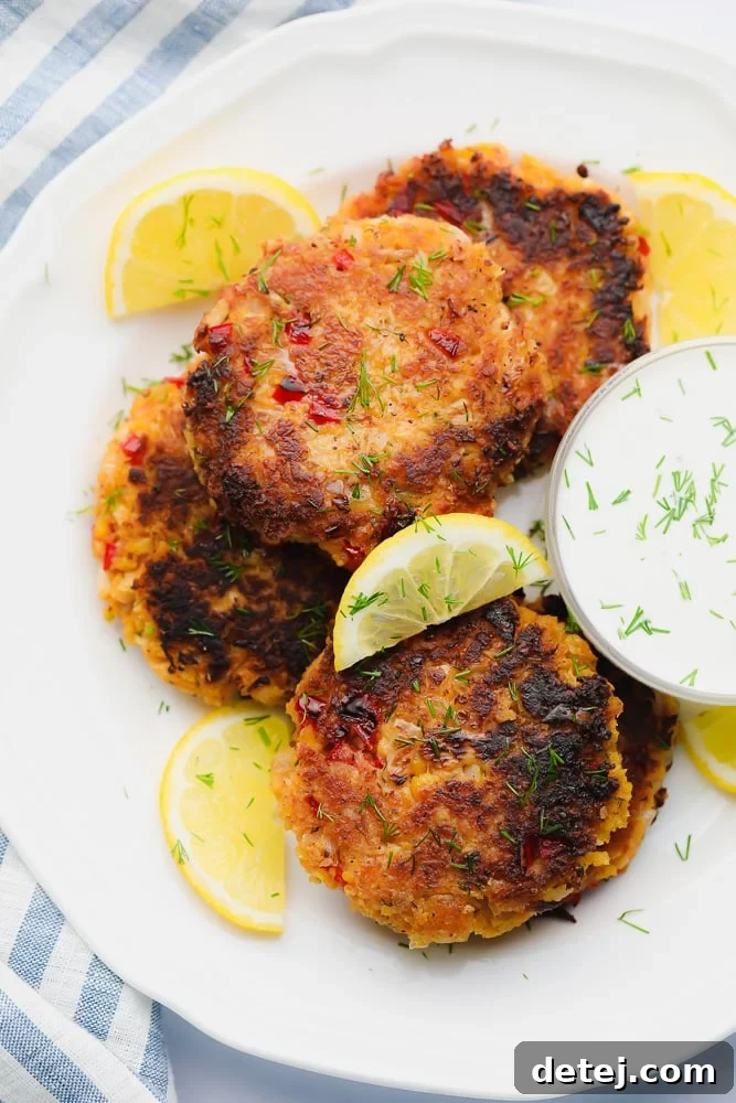 Golden brown vegan crab cakes on a white plate with lemon wedges and a side of creamy lemon aioli for dipping