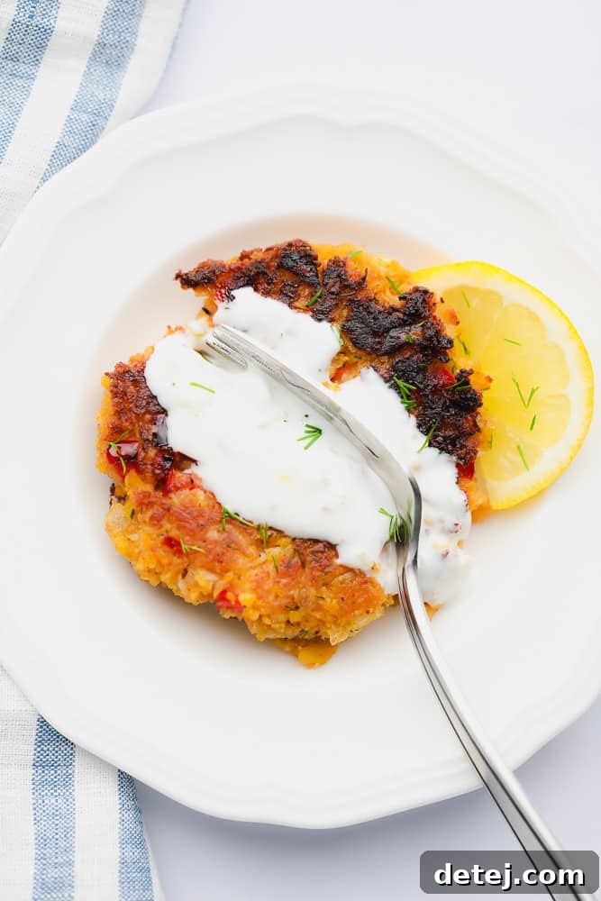 A fork gently breaking into a sauce-covered vegan crab cake, revealing its flaky, tender interior on a white plate