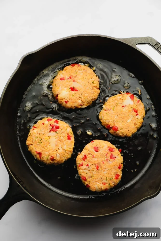 Close-up shot of vegan crab cakes sizzling and turning golden brown in a cast iron skillet