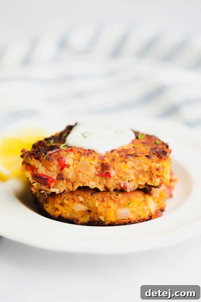 Two perfectly cooked vegan crab cakes stacked on top of each other, generously topped with a creamy white sauce
