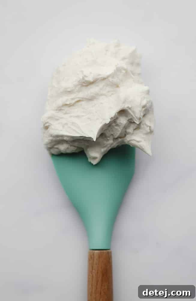 spatula with frosting on it, teal colored and white backdrop