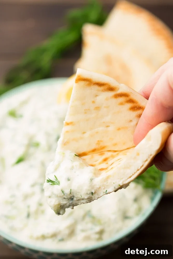 A close-up of warm, soft pita bread being dipped into a bowl of the creamy homemade vegan tzatziki sauce, highlighting its luscious texture.