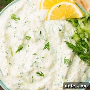 A vibrant image of a bowl of creamy vegan tzatziki, artfully garnished with fresh dill and lemon slices, inviting you to dip in.