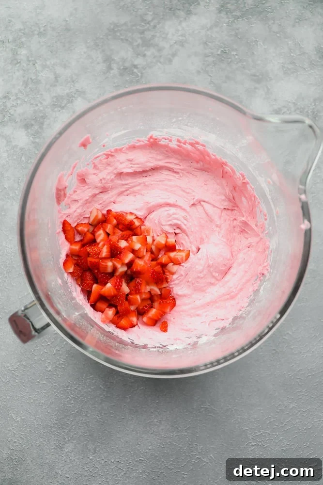 A bowl filled with vibrant pink vegan cupcake batter, visibly studded with small pieces of real strawberries.