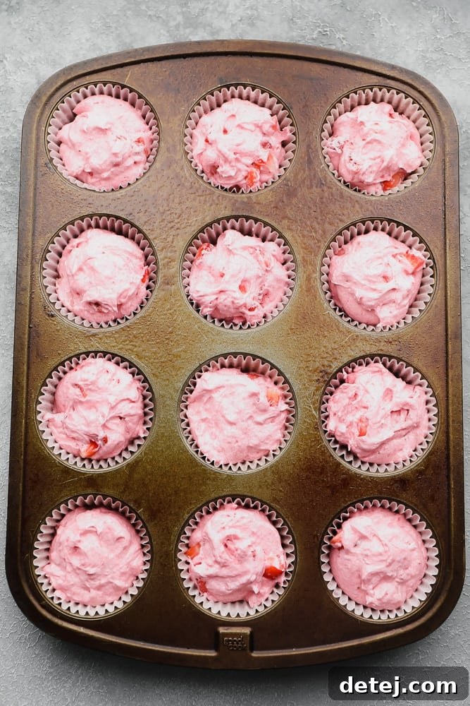 Close-up of a cupcake pan with paper liners, each filled three-quarters full with pink vegan strawberry cupcake batter.